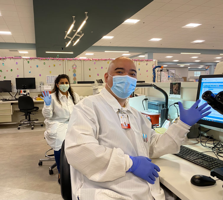 Two medical professionals with gloves smiling and waving